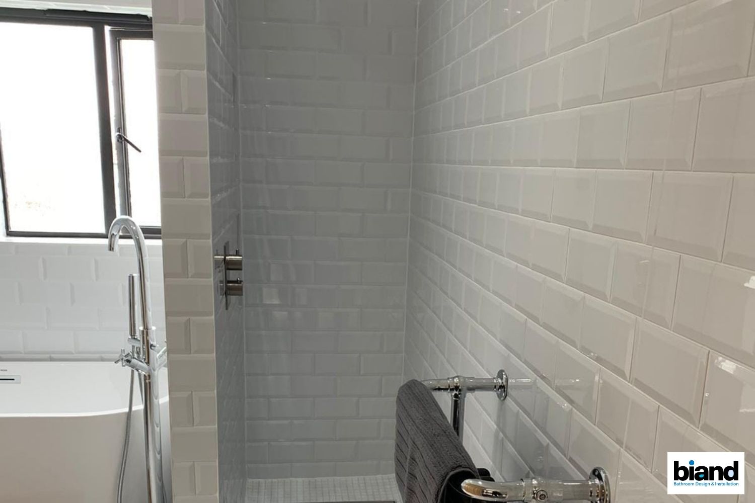 White tiled shower and bathroom with a window and a towel rack.