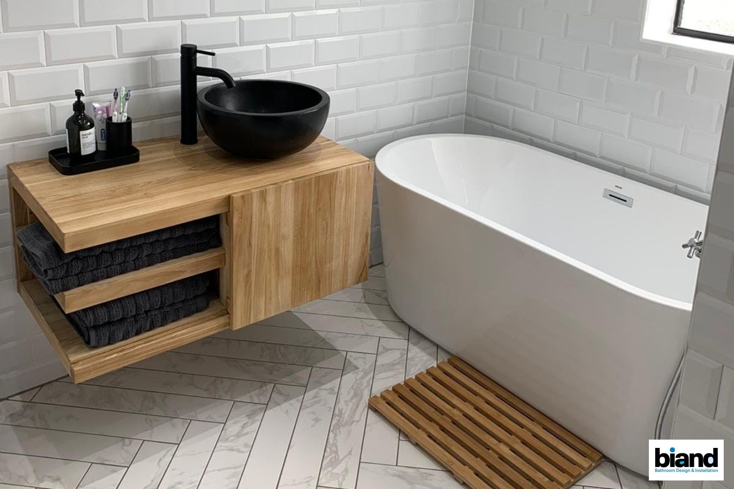 Modern bathroom with wooden vanity and black sink, white tub, and tile.