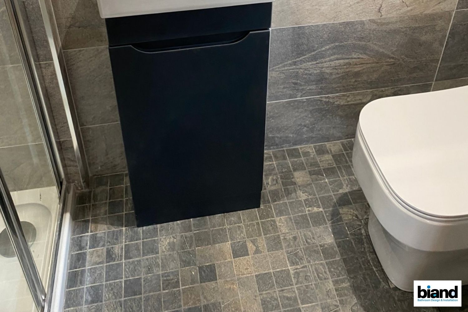Bathroom with a dark blue cabinet, gray floor tiles, and a white toilet.