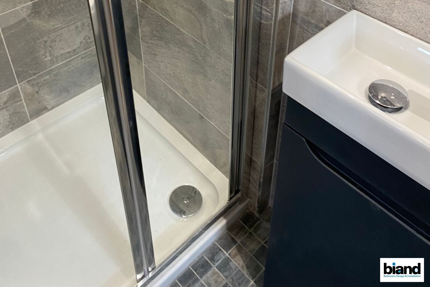 Shower with a dark blue vanity and white sink, tiles in shades of grey.
