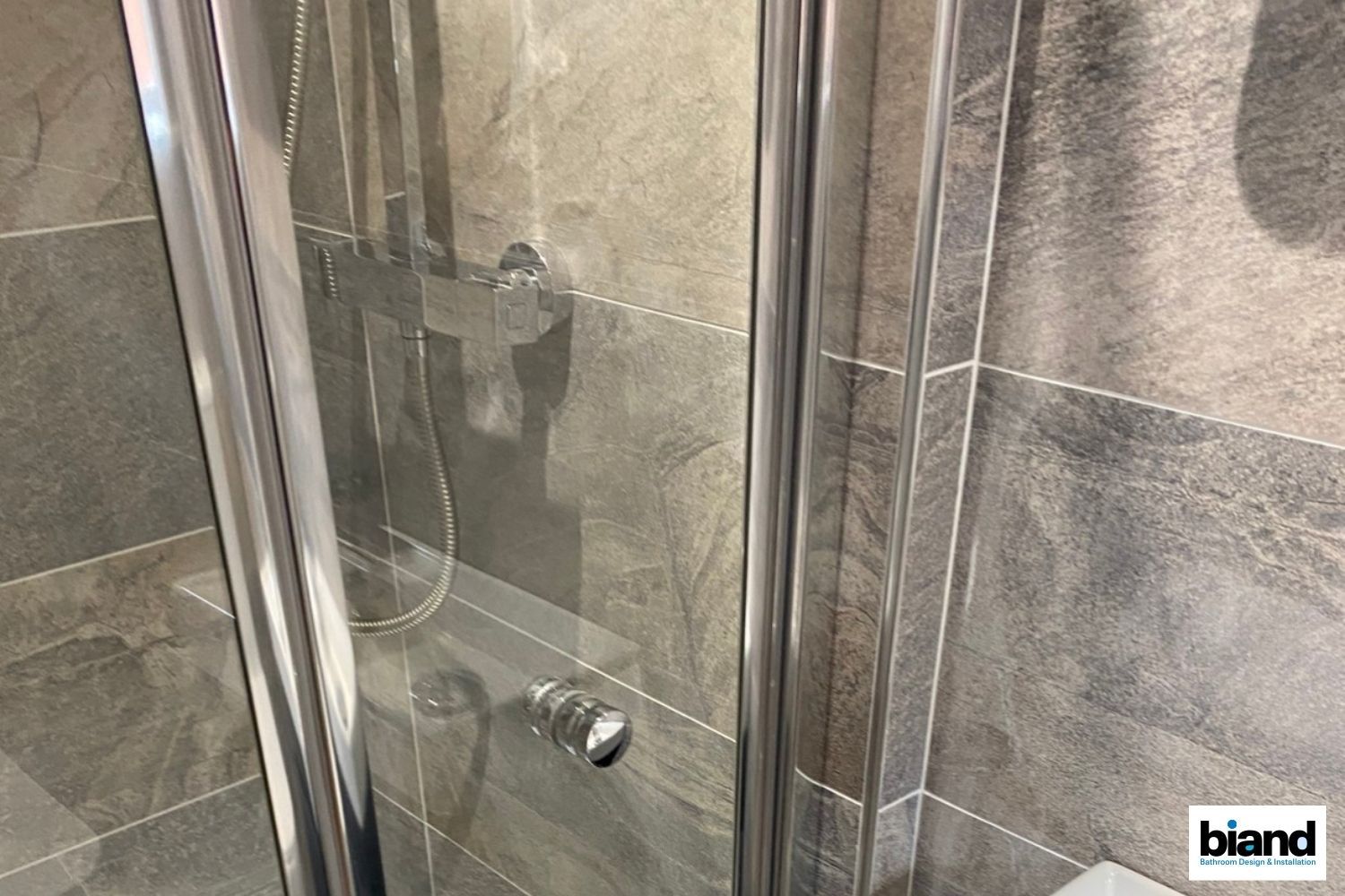 Shower stall with glass door, silver fixtures, and gray tiled walls.