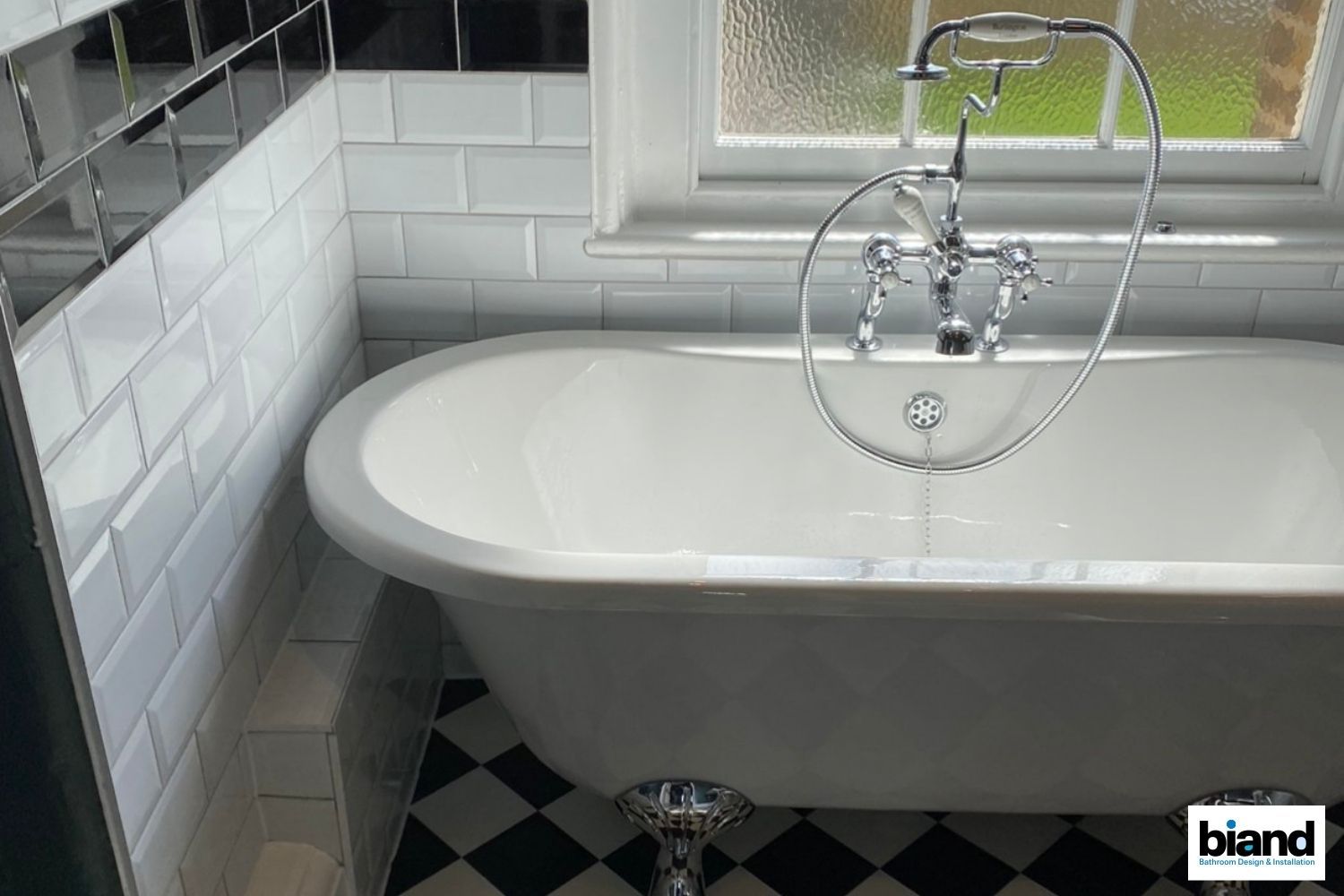 Claw-foot tub in a bathroom with white subway tile, a black and white checkered floor, and chrome fixtures.