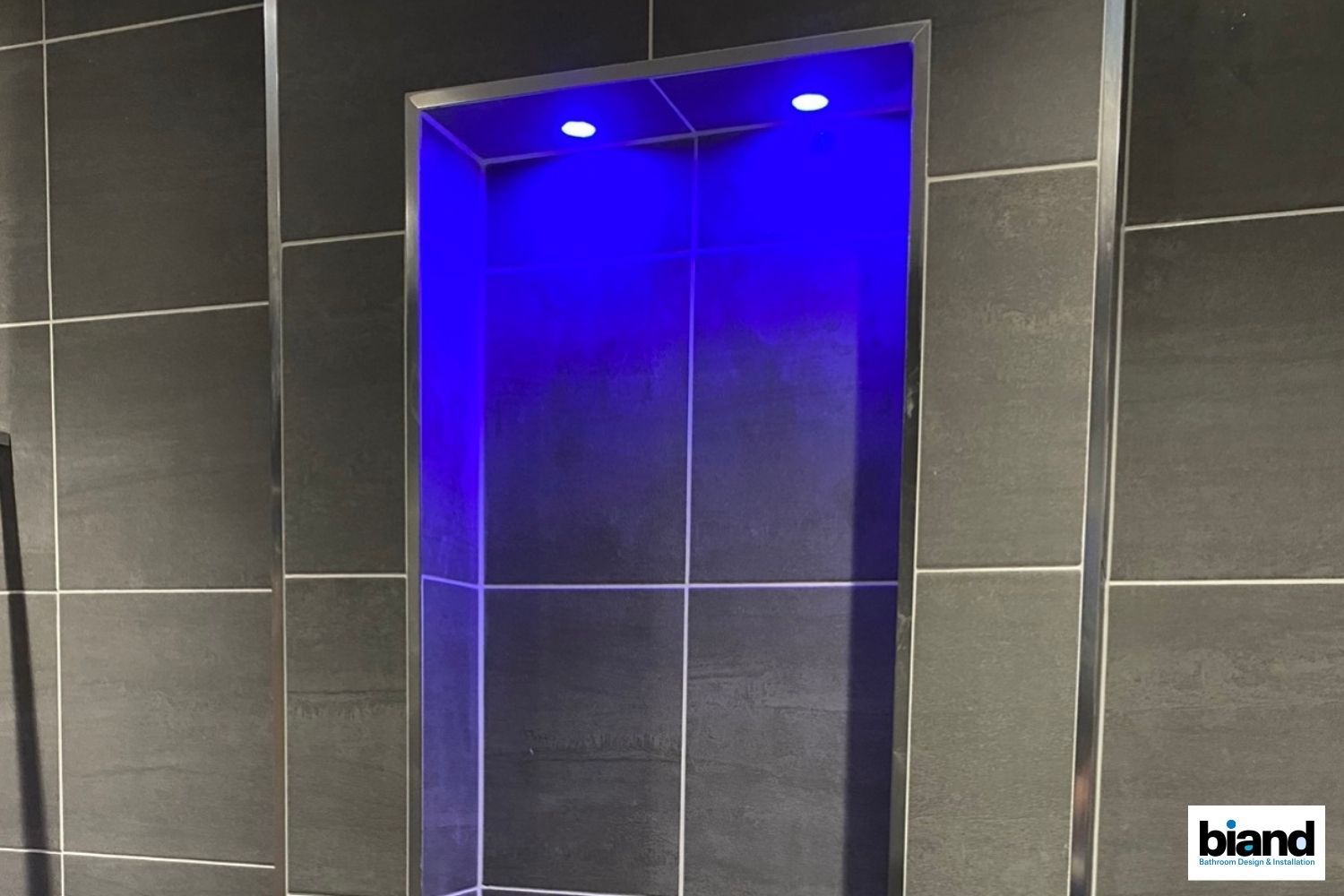 Recessed bathroom shelf with blue lighting, gray tiles, and silver trim.