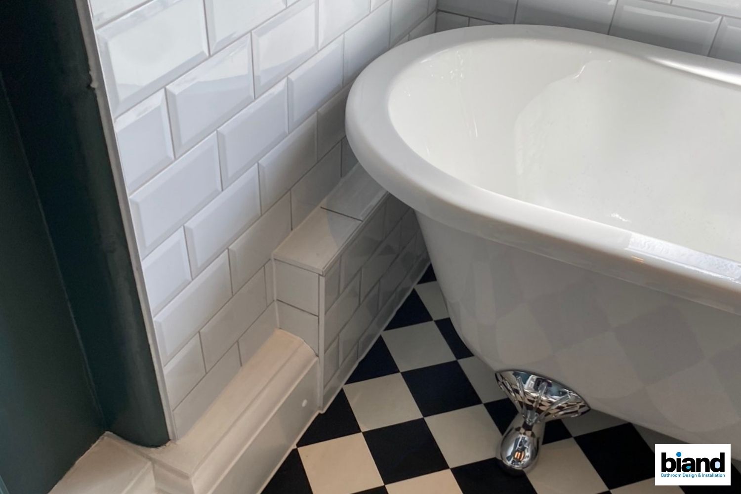 Corner of a bathroom with white subway tile, black and white checkered floor, and a clawfoot bathtub.