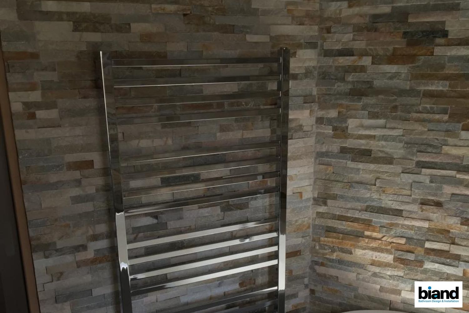 Chrome towel warmer on a stone-tiled wall.