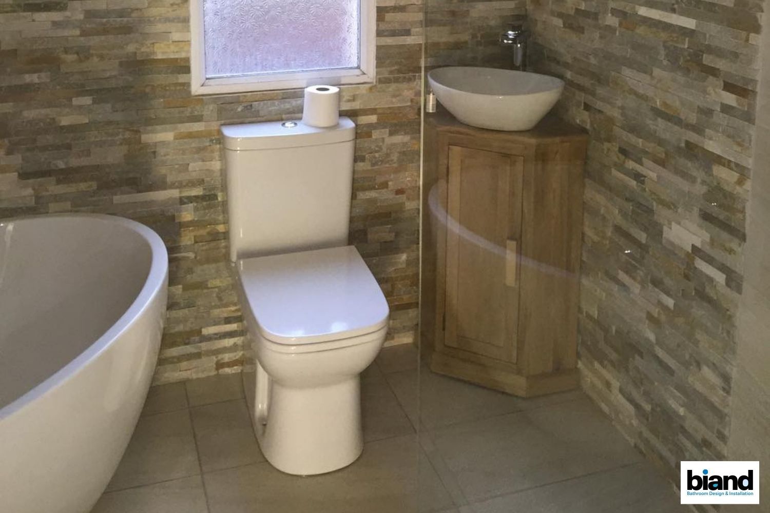 Bathroom with a white toilet, vessel sink, and stone-textured walls. Bathtub on left.