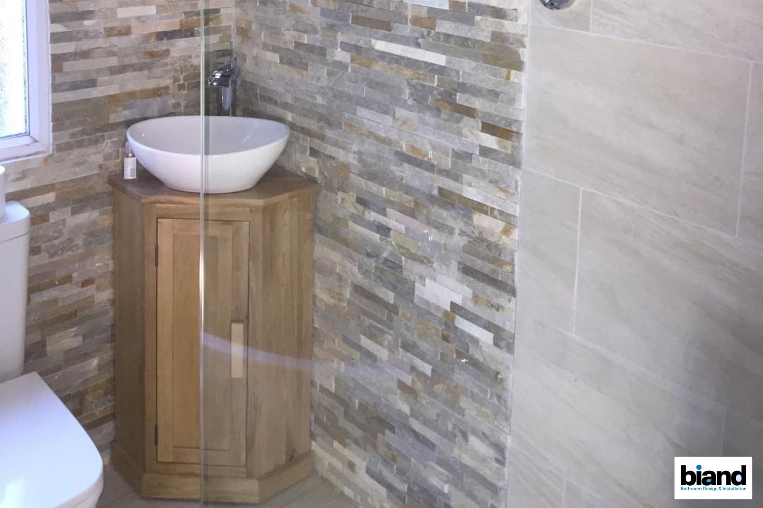 Bathroom with stone accent wall, wooden vanity with vessel sink, and shower stall.