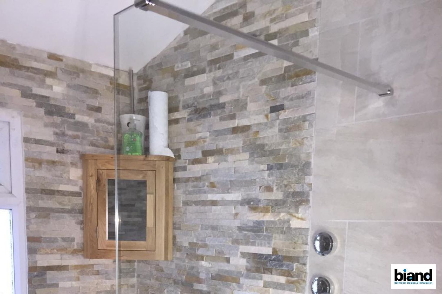 Shower with stone accent wall, glass divider, wooden cabinet, and chrome fixtures.