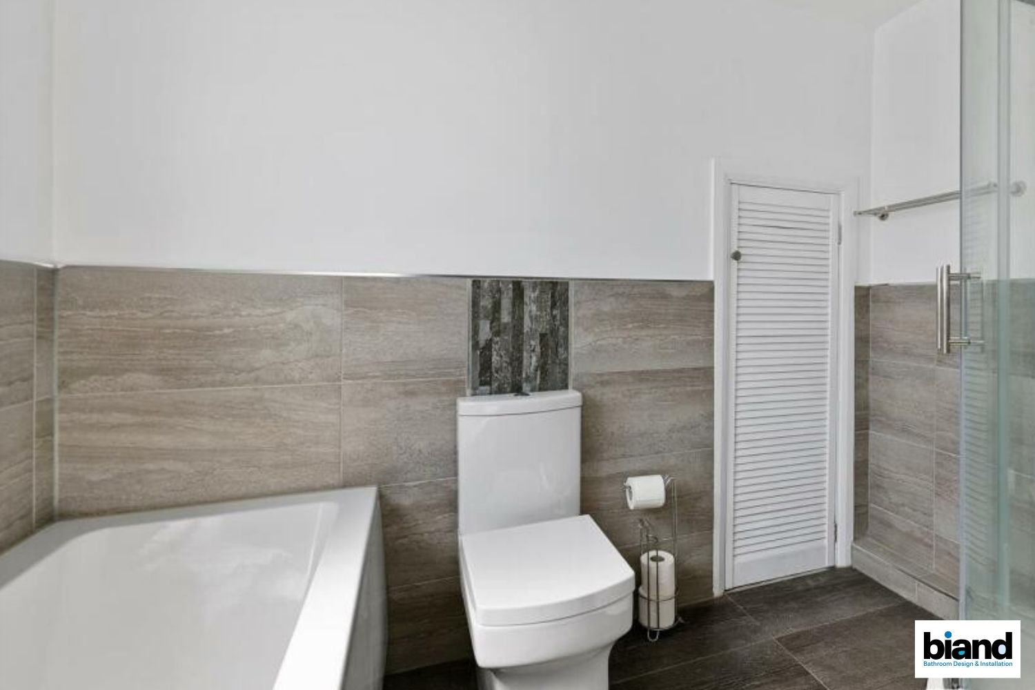 Bathroom with a white toilet, tub, and door; gray tile and wall.