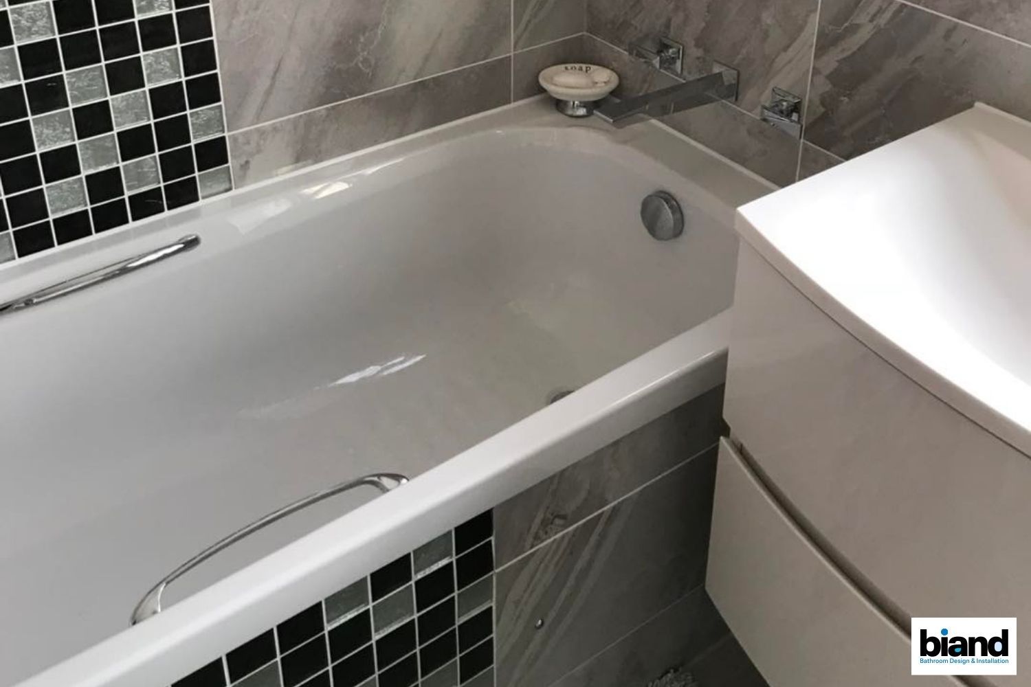 Bathtub with chrome accents, contrasting tile, and a white vanity in a modern bathroom setting.