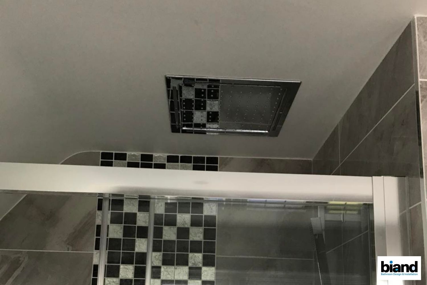 Shower with overhead rain showerhead, black & white tile accent, gray walls, and a glass sliding door.