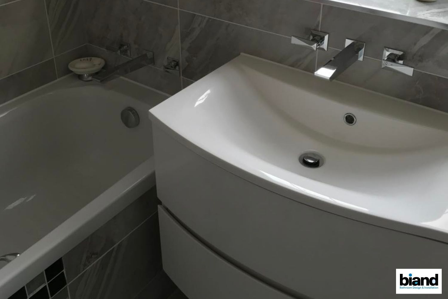 White bathroom sink and bathtub in a modern bathroom with gray tiles.