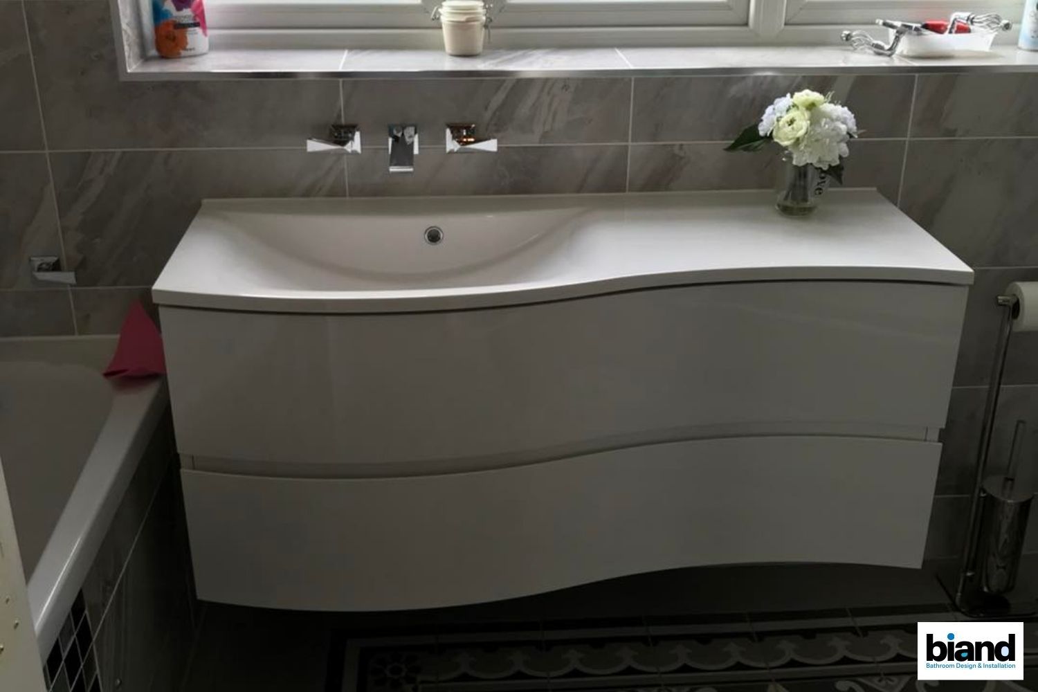 White, curved-front bathroom vanity with a sink, mounted on the wall, below a window.