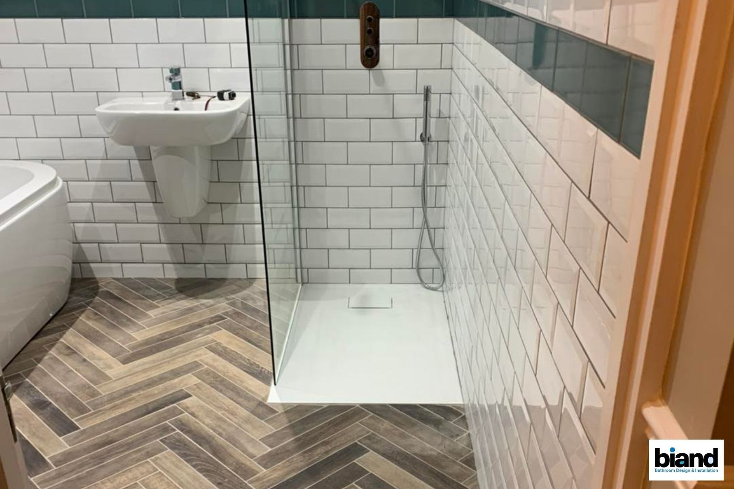 Bathroom with herringbone floor, white subway tile walls, glass shower, and pedestal sink.