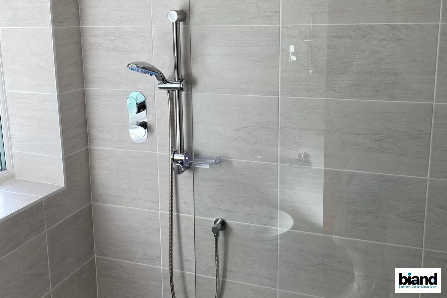 Shower stall with chrome fixtures, light gray tiles, and a glass door.