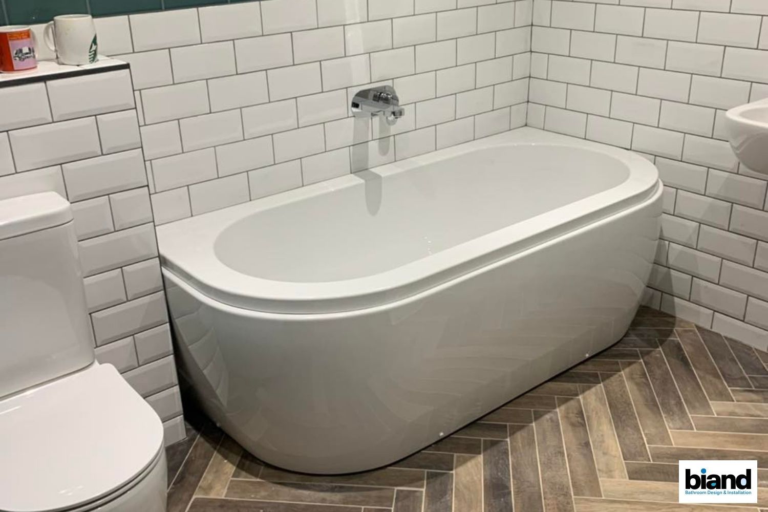 White freestanding bathtub in a bathroom with subway tile walls and herringbone tile floor.