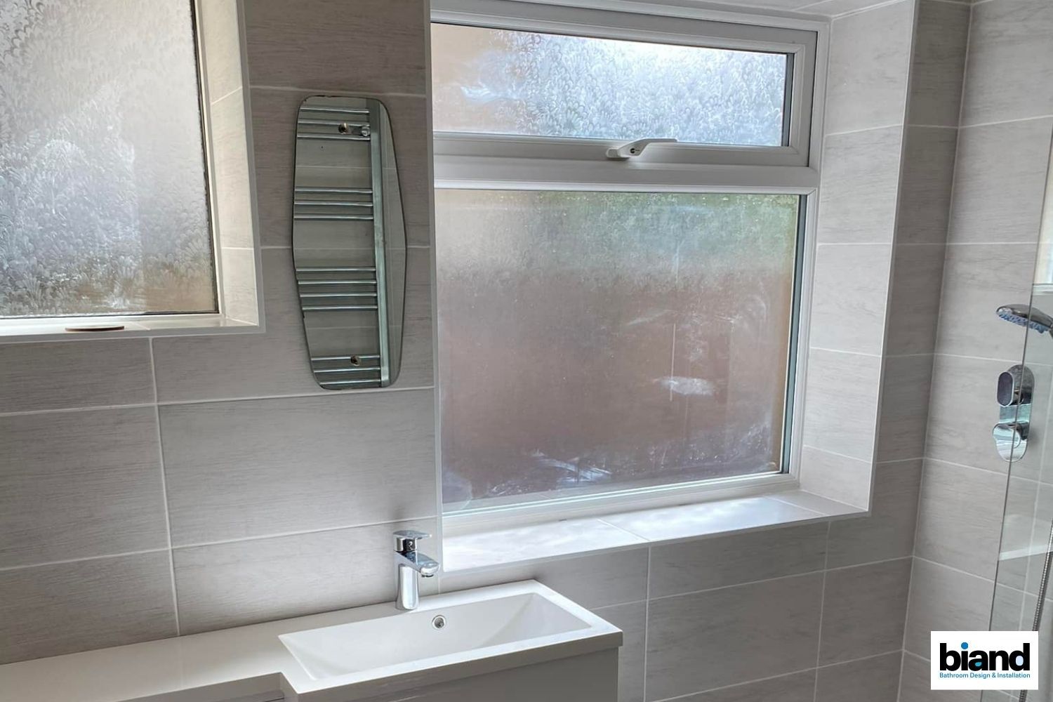 Bathroom with a frosted window, a white sink, and light gray tile walls.