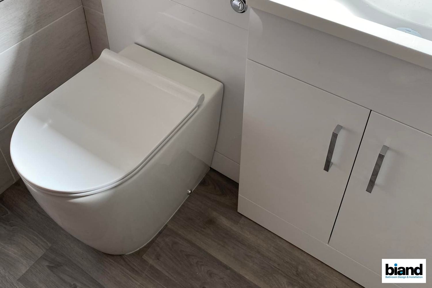 Modern white toilet and cabinet in a bathroom with gray wood-look flooring.