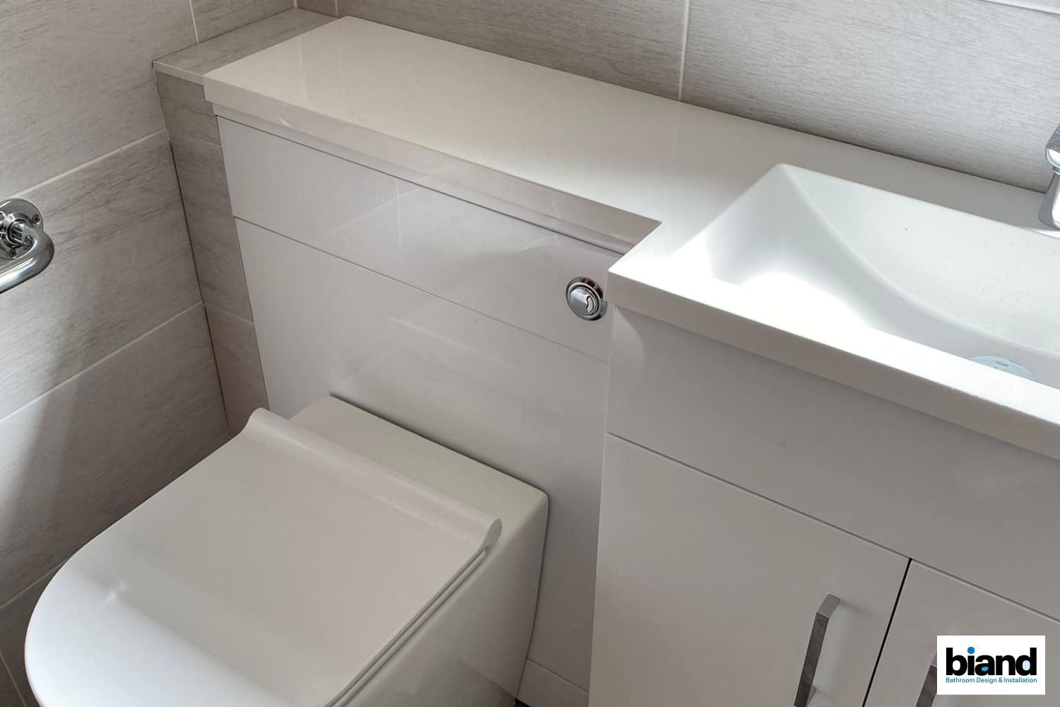 Toilet and sink combined in a compact white and gray bathroom with a built-in cabinet.