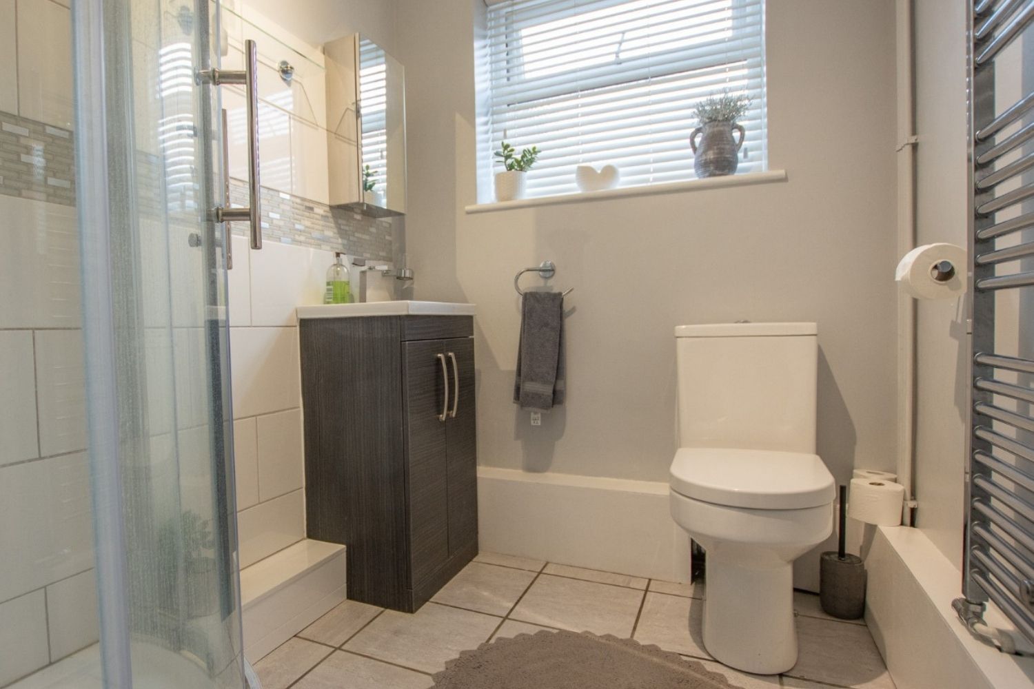 Bathroom with shower, toilet, vanity, and window. Gray, white, and neutral colors.