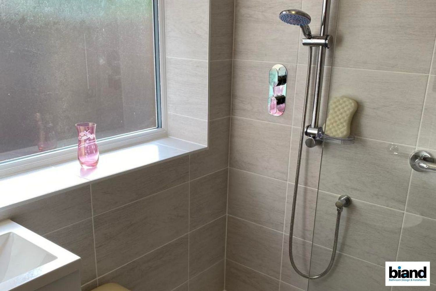 Shower stall with light-colored tiled walls, a window, and a showerhead.