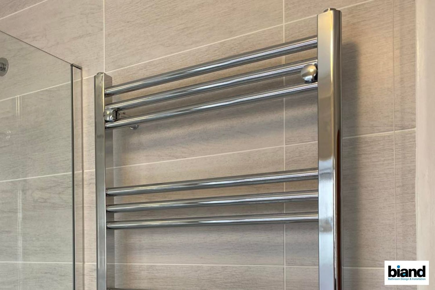 Silver towel warmer mounted on a tiled wall next to a shower door.