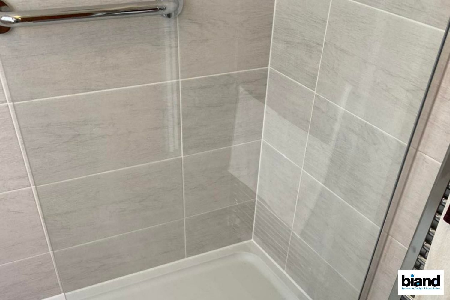 Shower stall with gray tile walls and a white shower tray.