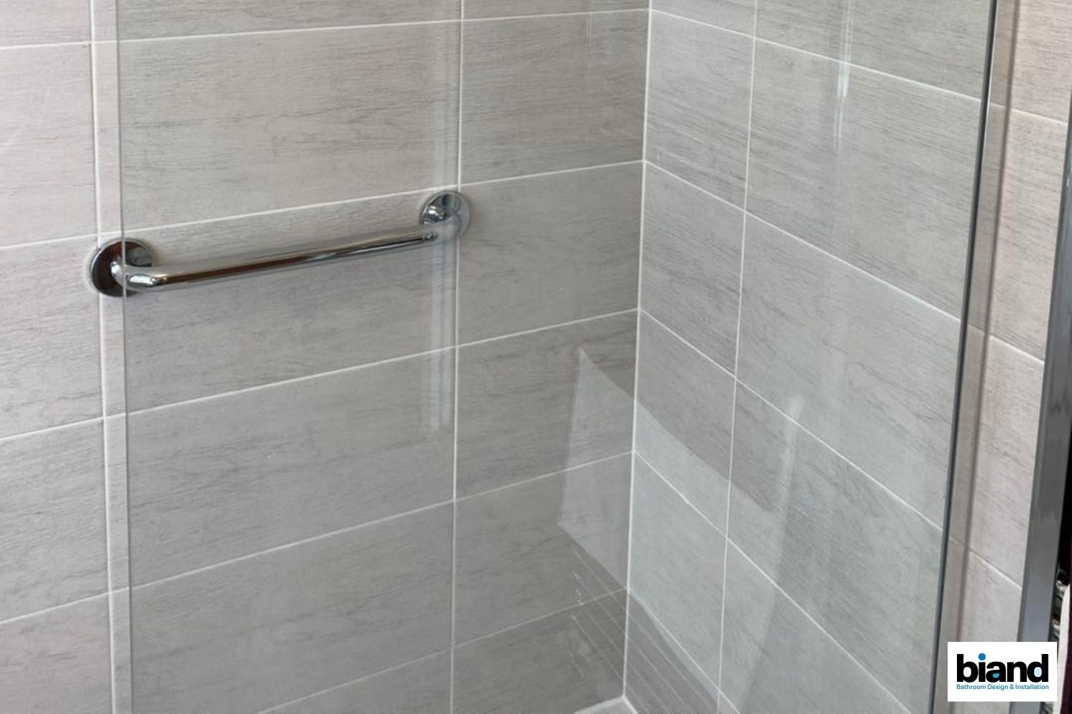 Gray tiled shower with a chrome grab bar.