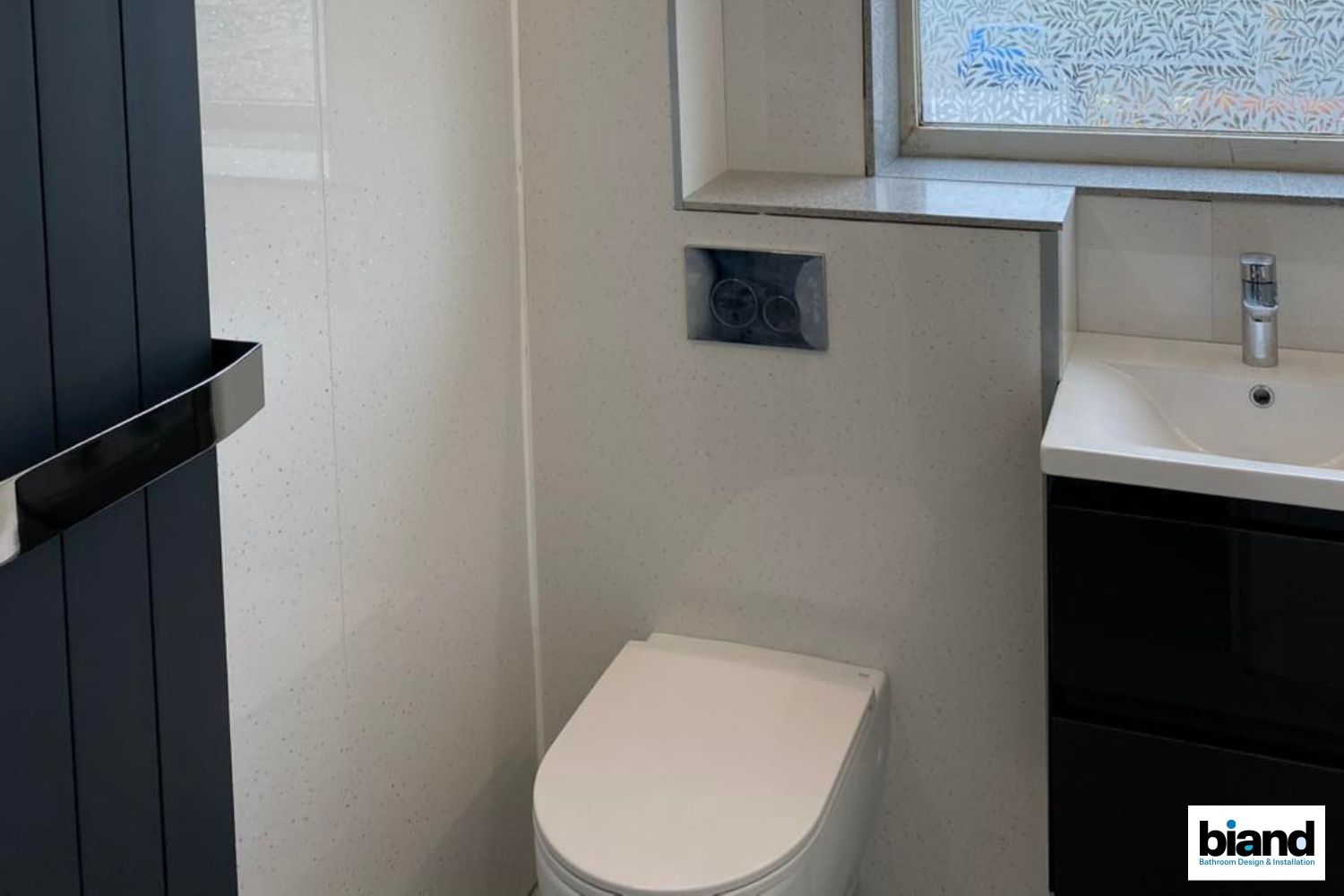 A small bathroom with a toilet, sink, and towel rack. The walls are light and dark grey.
