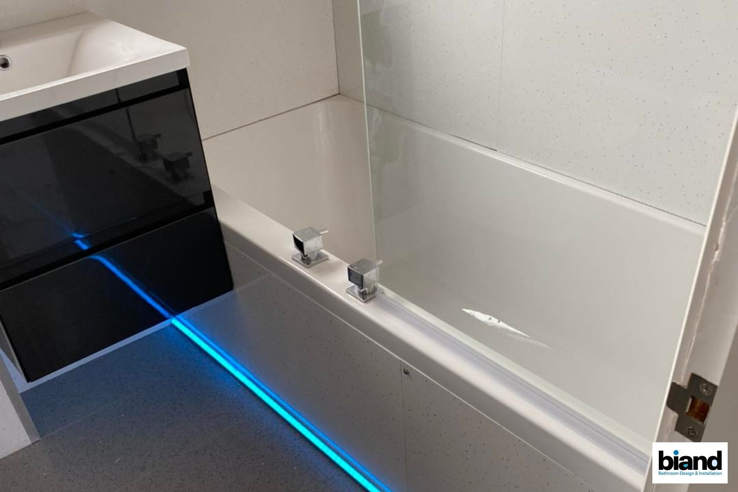Modern bathroom with a white bathtub, a glass shower screen, a black vanity, and blue LED lighting.