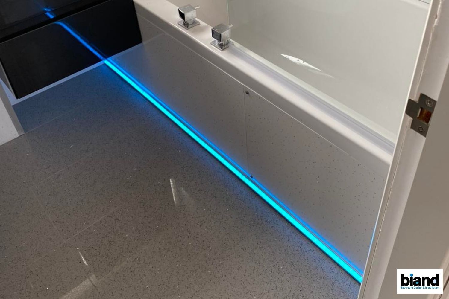 Bathroom with blue LED strip lighting along the base of a white tub. Gray floor.