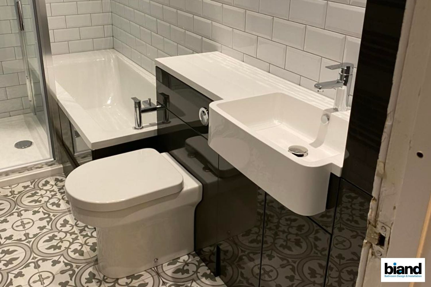 Bathroom with white fixtures, gray vanity, black wall, patterned floor, and subway tile.