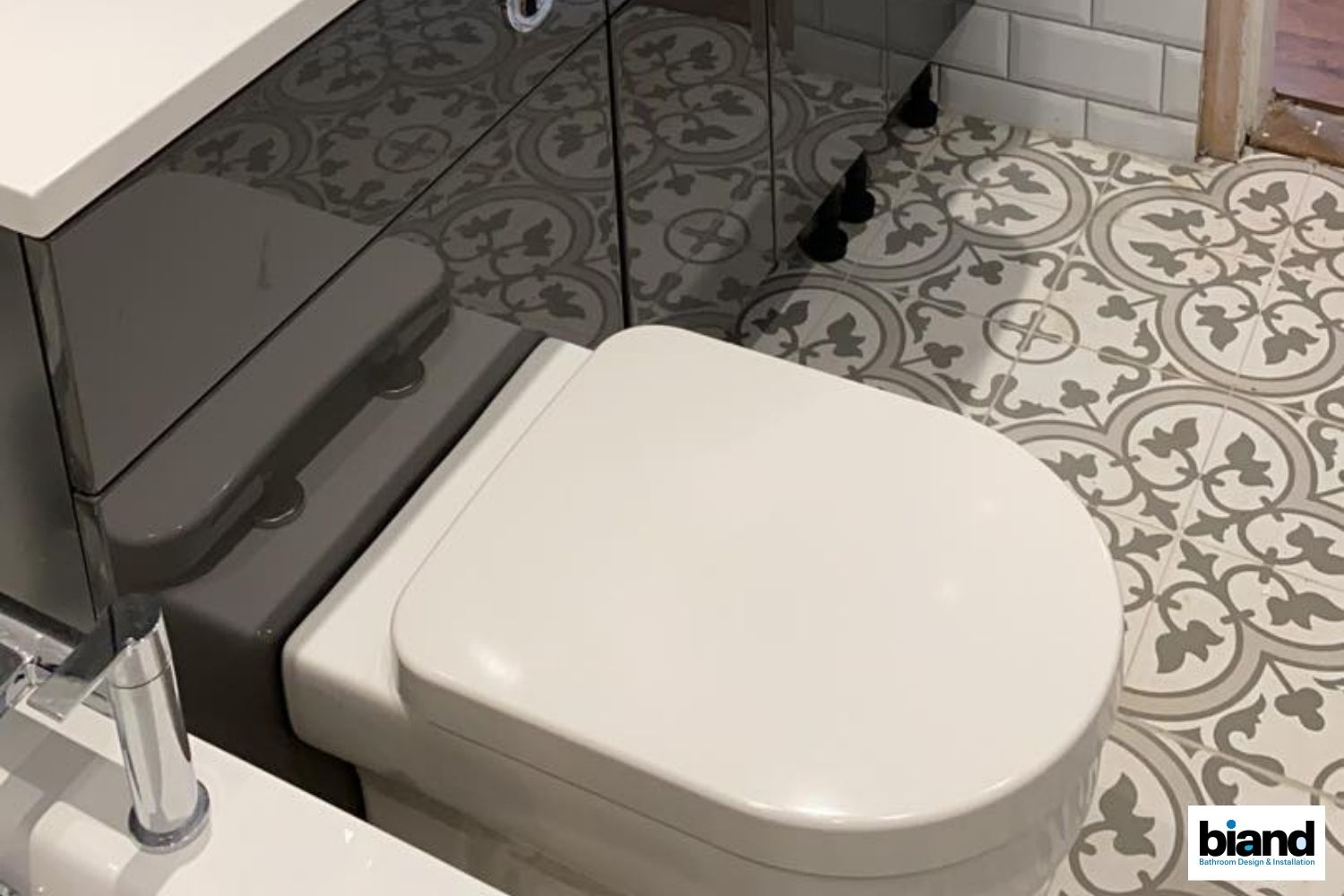Bathroom with patterned floor tiles, a gray cabinet, and a white toilet.