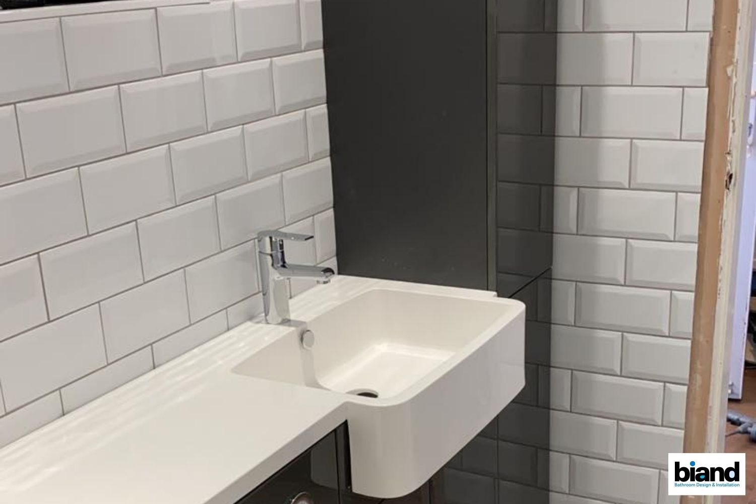A modern white bathroom sink and faucet against white subway tile and a dark gray wall.