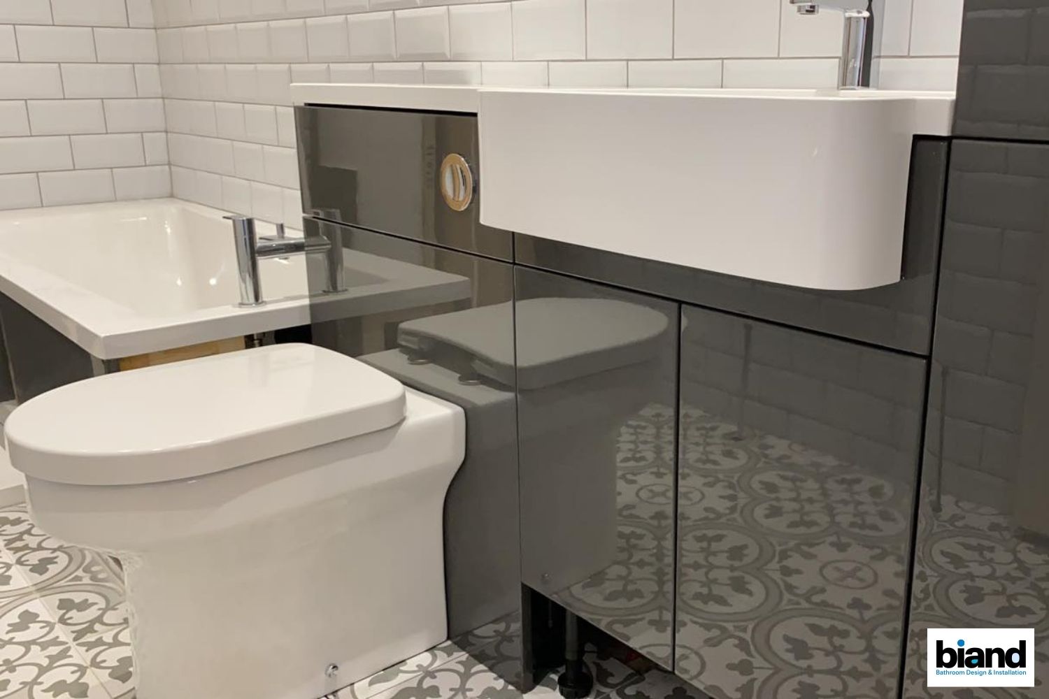 Modern bathroom: grey cabinets, white toilet and sink, bathtub, patterned floor.