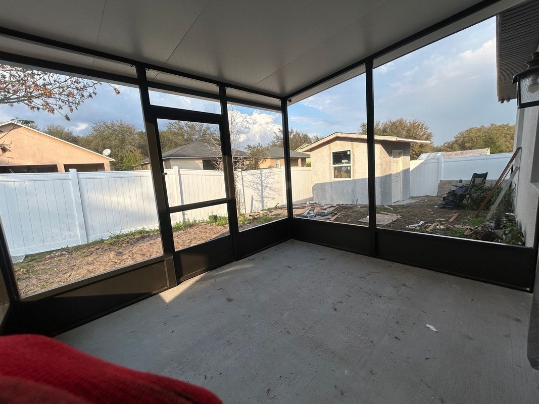An empty screened in porch with a red blanket on the floor