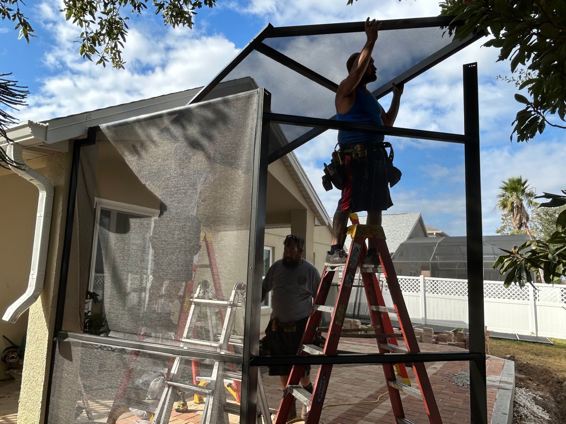 Two men are working on a greenhouse in front of a house