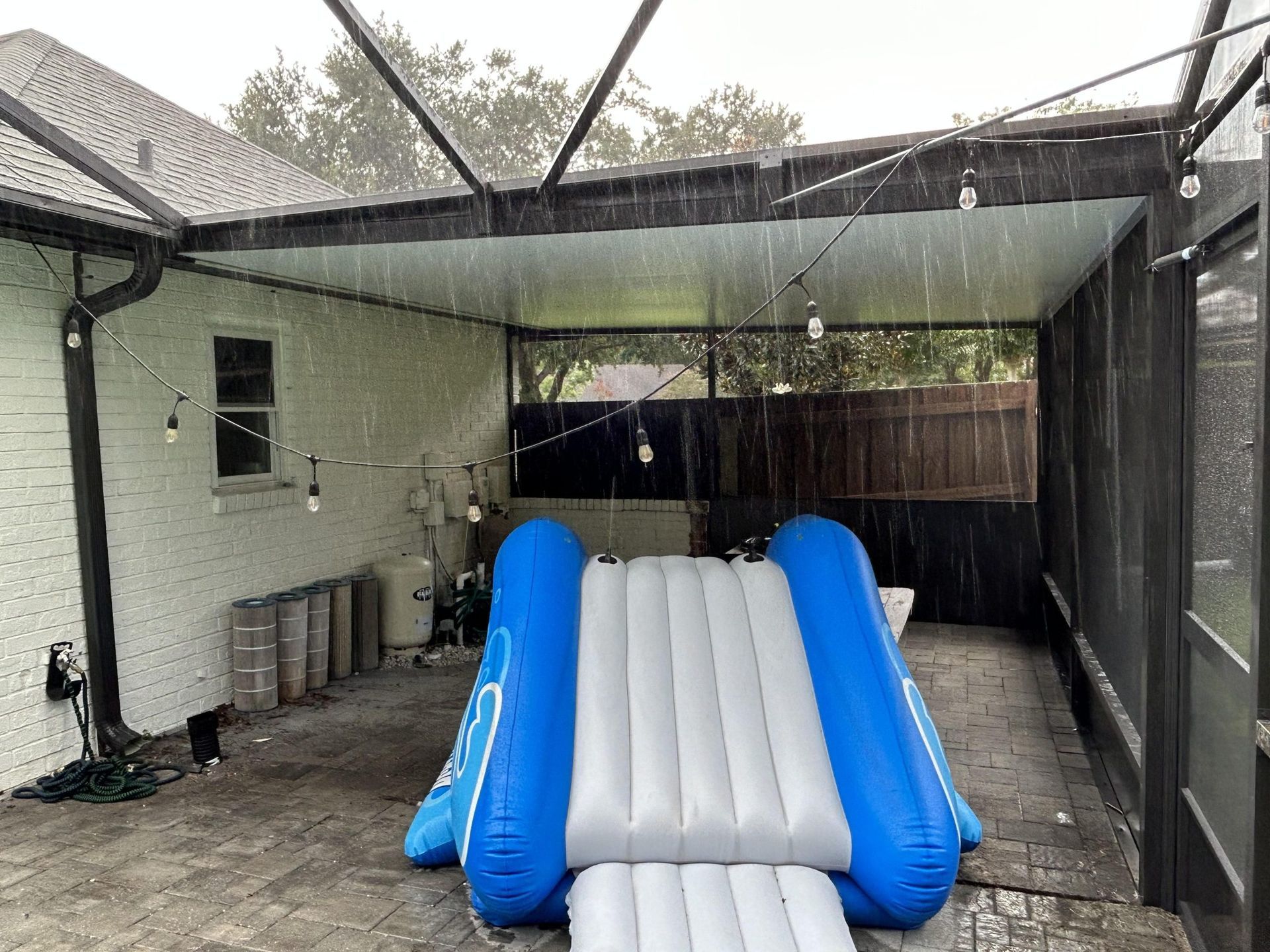 A blue and gray inflatable slide is sitting in the backyard of a house