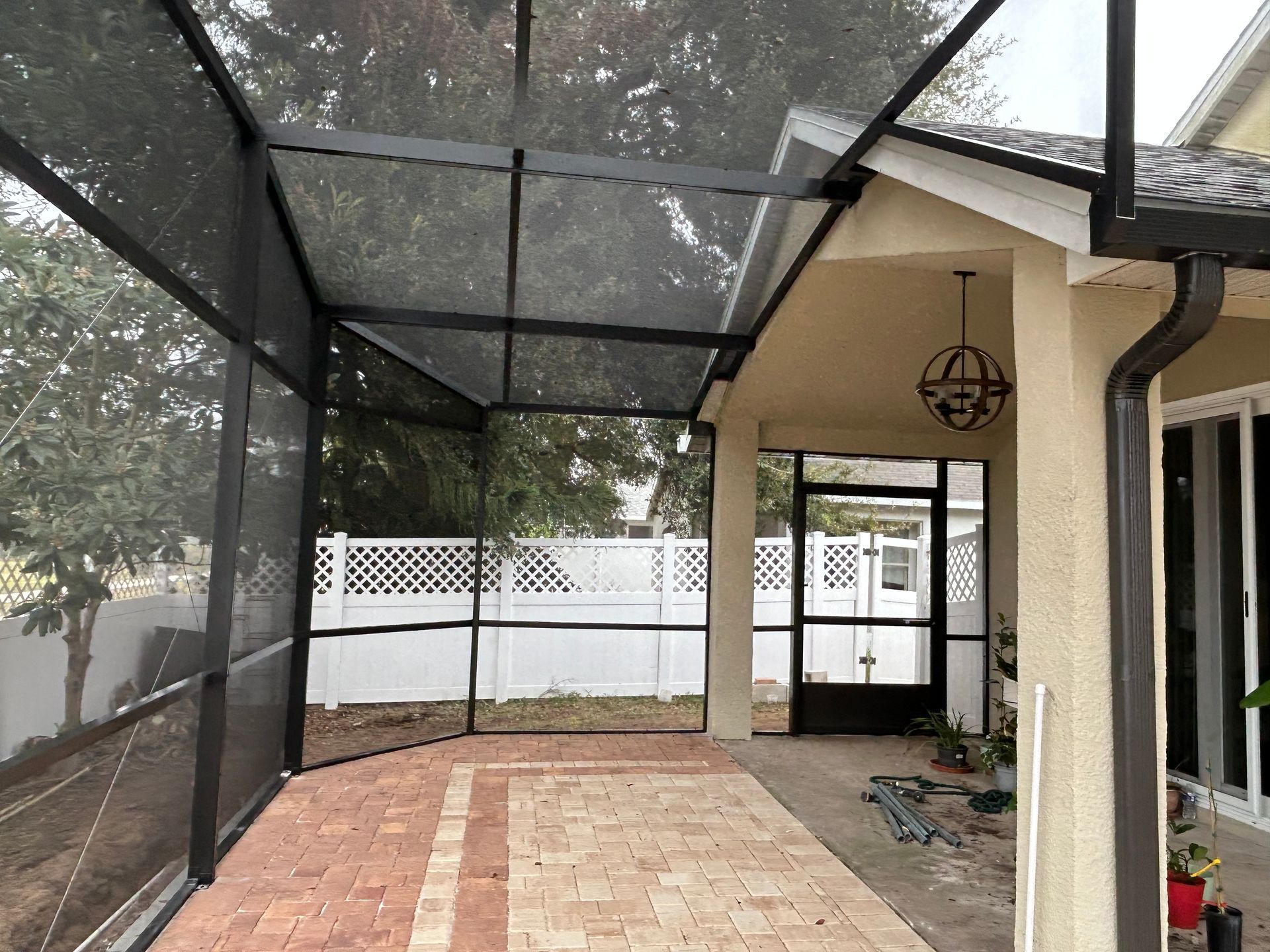 A screened in porch with a brick walkway and a white fence