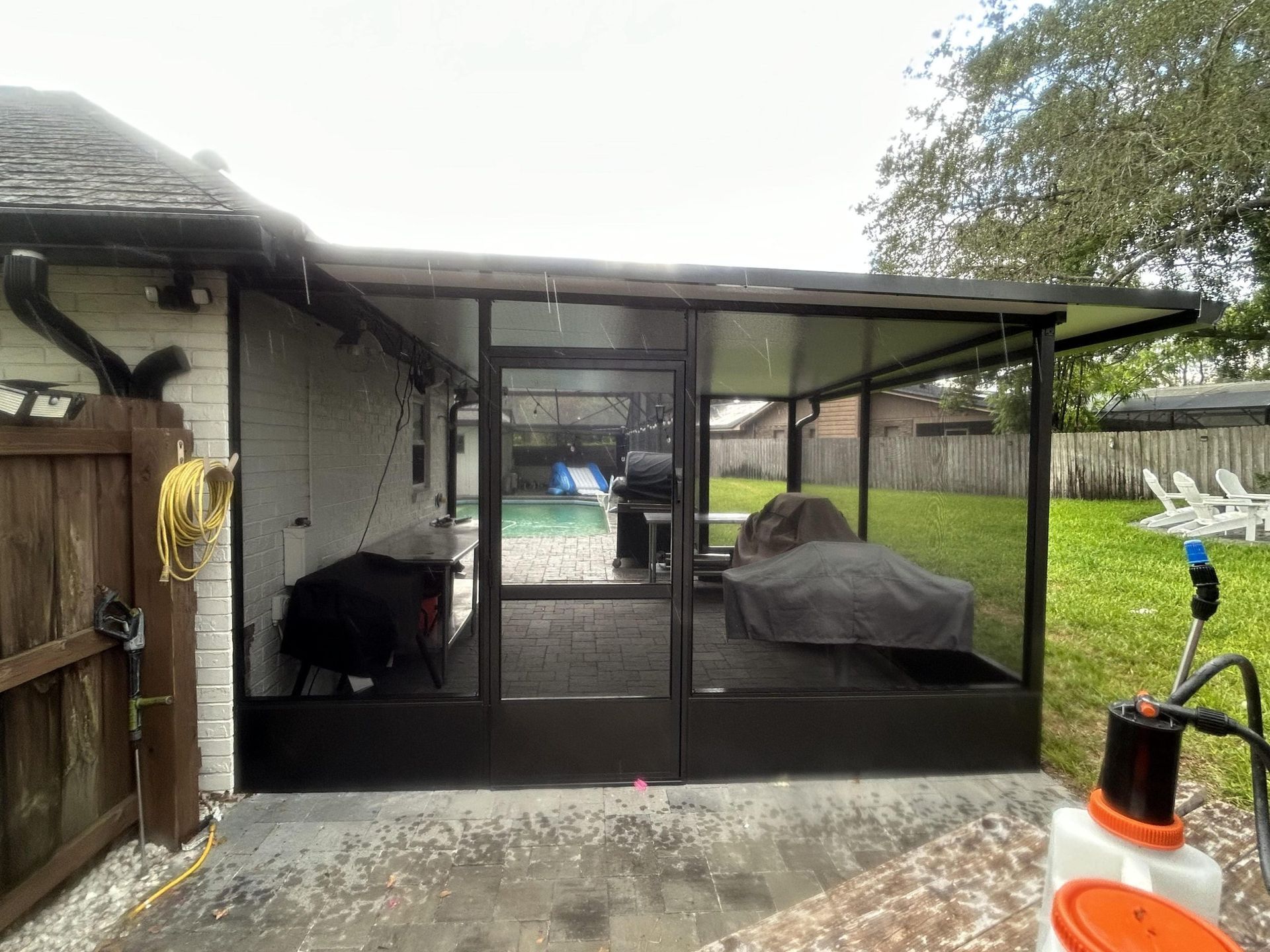 A screened in porch with a grill and a lawn mower in the backyard of a house