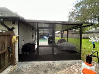 A screened in porch with a grill and a lawn mower in the backyard of a house