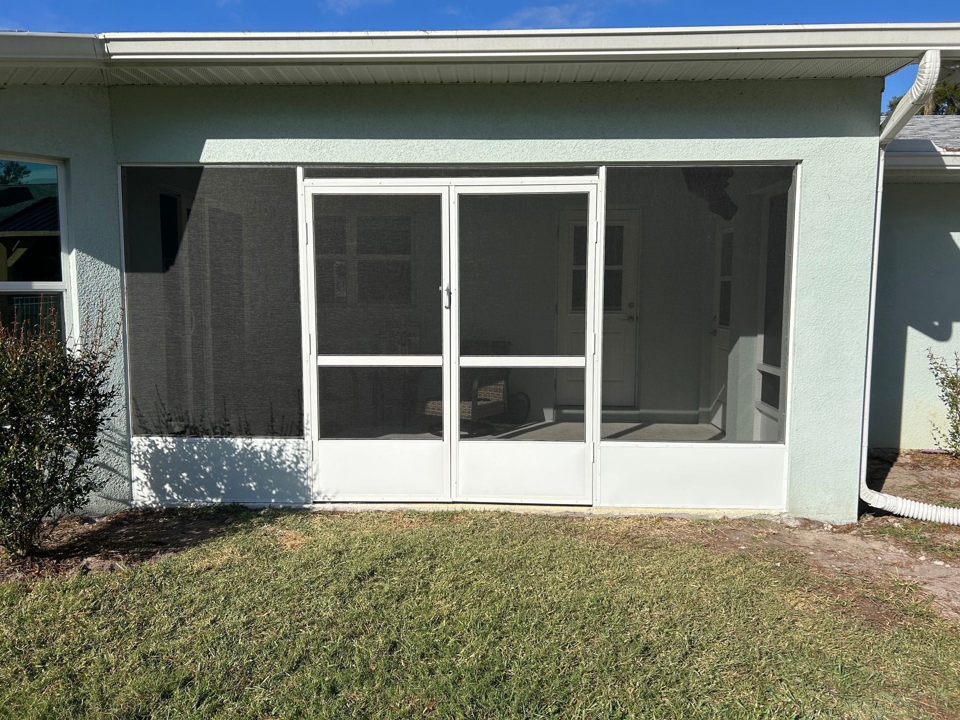 A screened in porch with sliding glass doors on the side of a house
