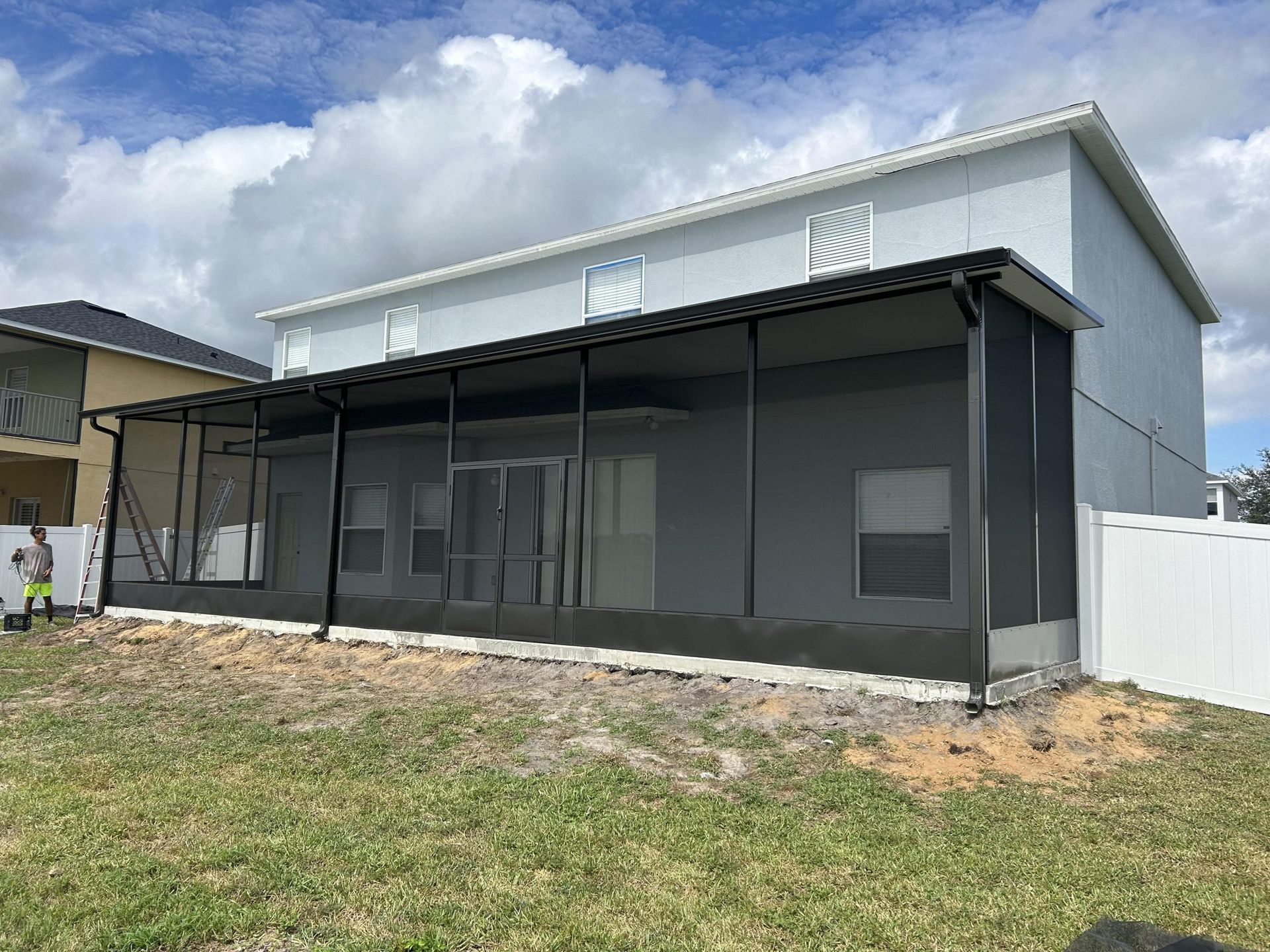 The back of a house with a screened in porch and a white fence
