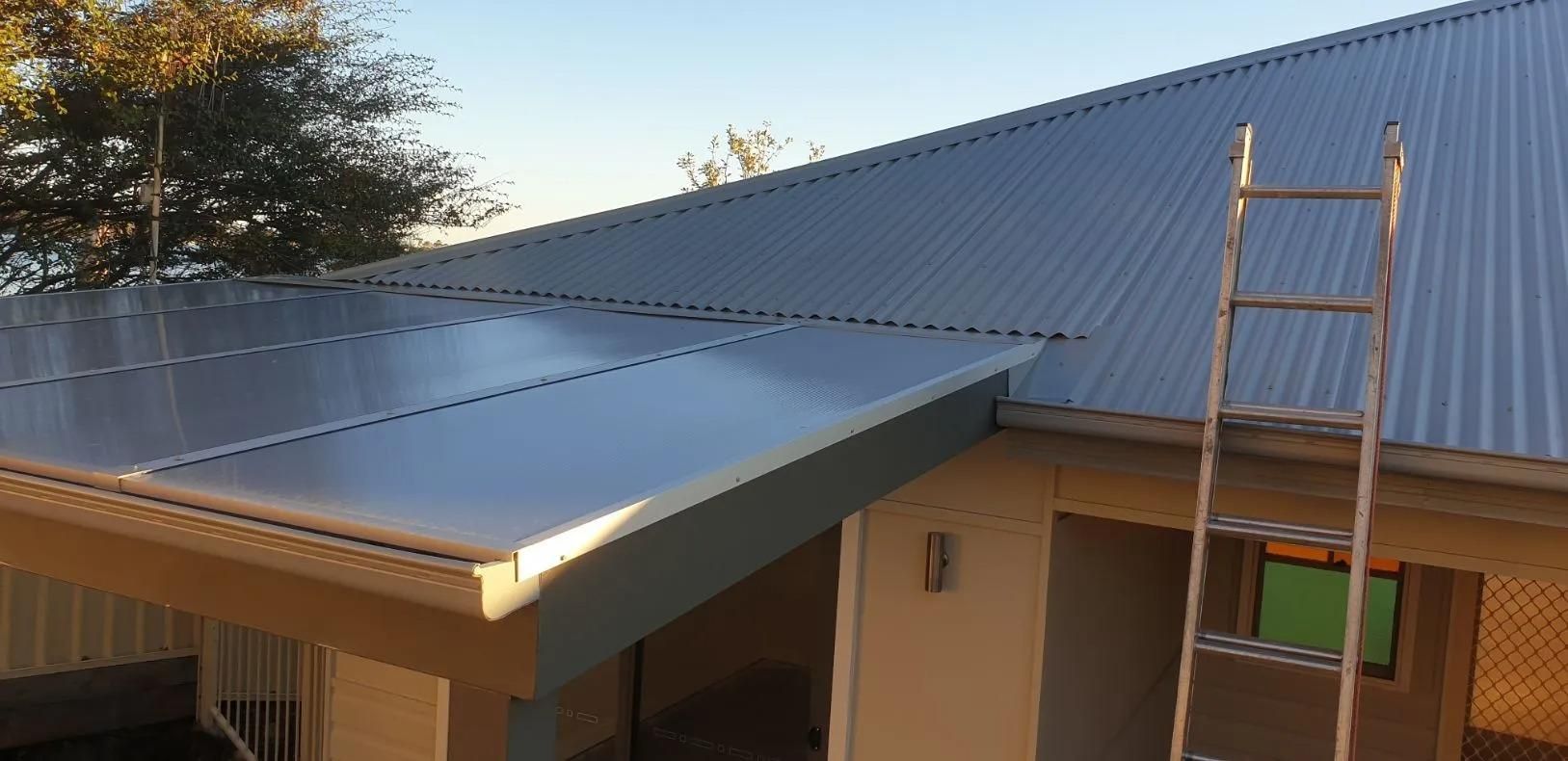 A Ladder is Sitting on the Roof of a House — Coast Metal Roof & Gutter In Tumbi Umbi, NSW