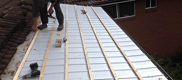 A Man is Working on the Roof of a House — Coast Metal Roof & Gutter In Tumbi Umbi, NSW