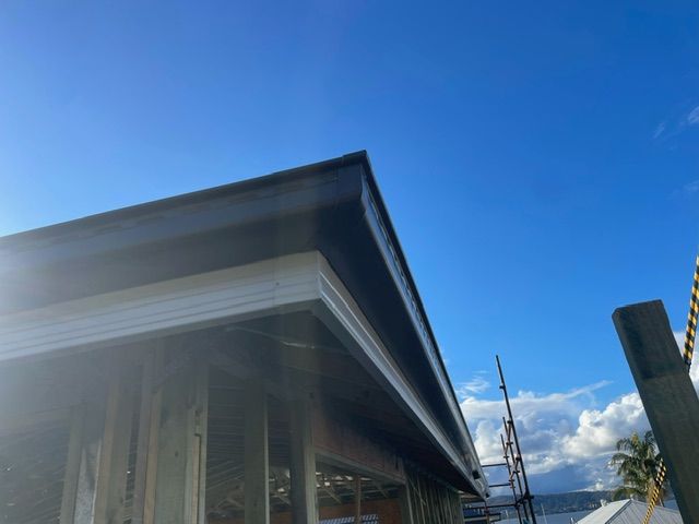 Gutter of a building with dark roof and blue sky — Coast Metal Roof & Gutter In Tumbi Umbi, NSW