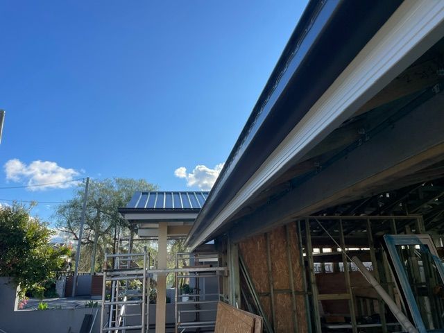 A Person is Installing a White Gutter on the Side of a Building — Coast Metal Roof & Gutter In Tumbi Umbi, NSW
