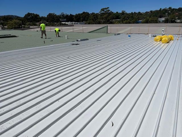 A grey roof attached to a green roof with men standing on top of it — Coast Metal Roof & Gutter In Tumbi Umbi, NSW