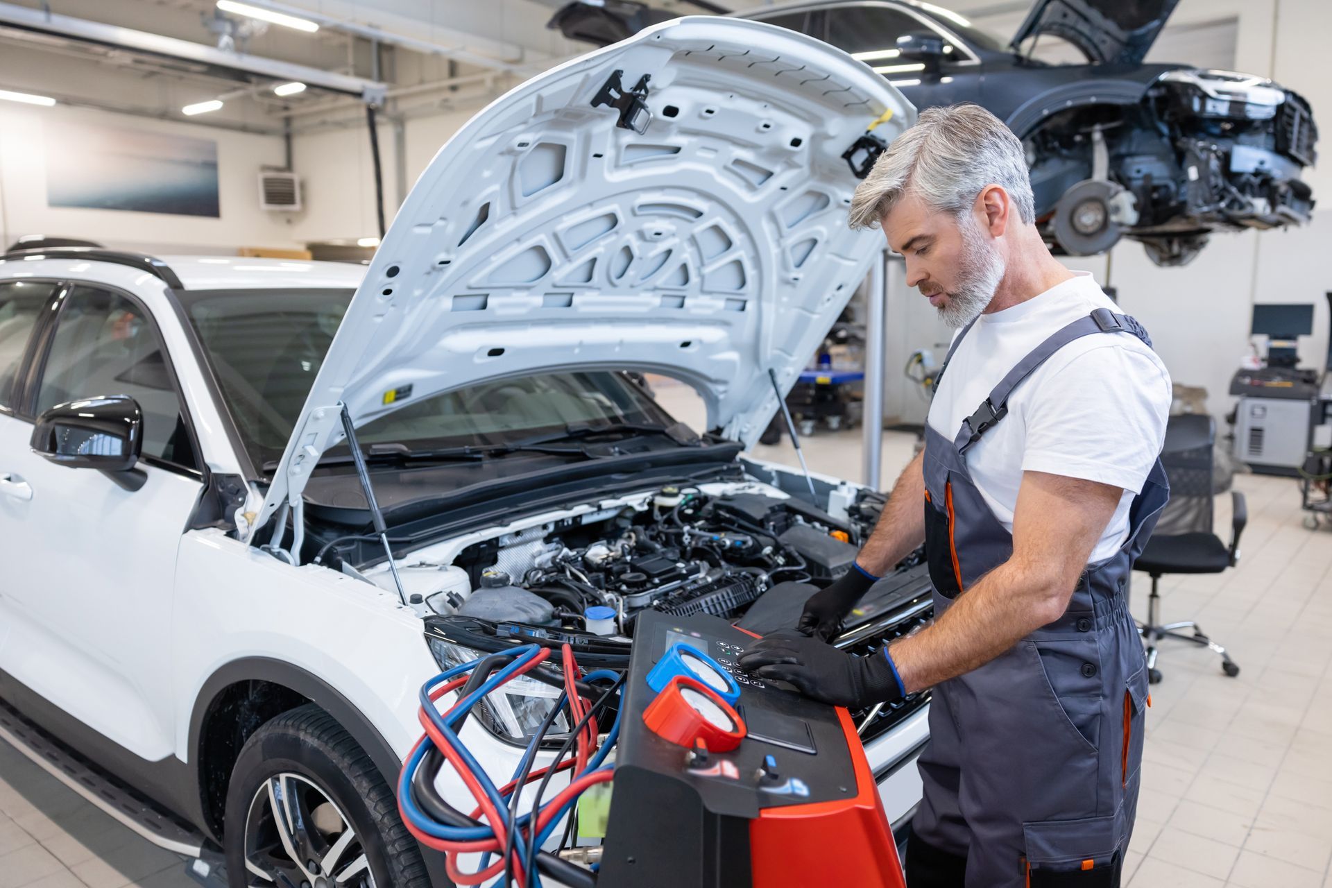 Mechanic working on a white car with hood open in an auto repair shop