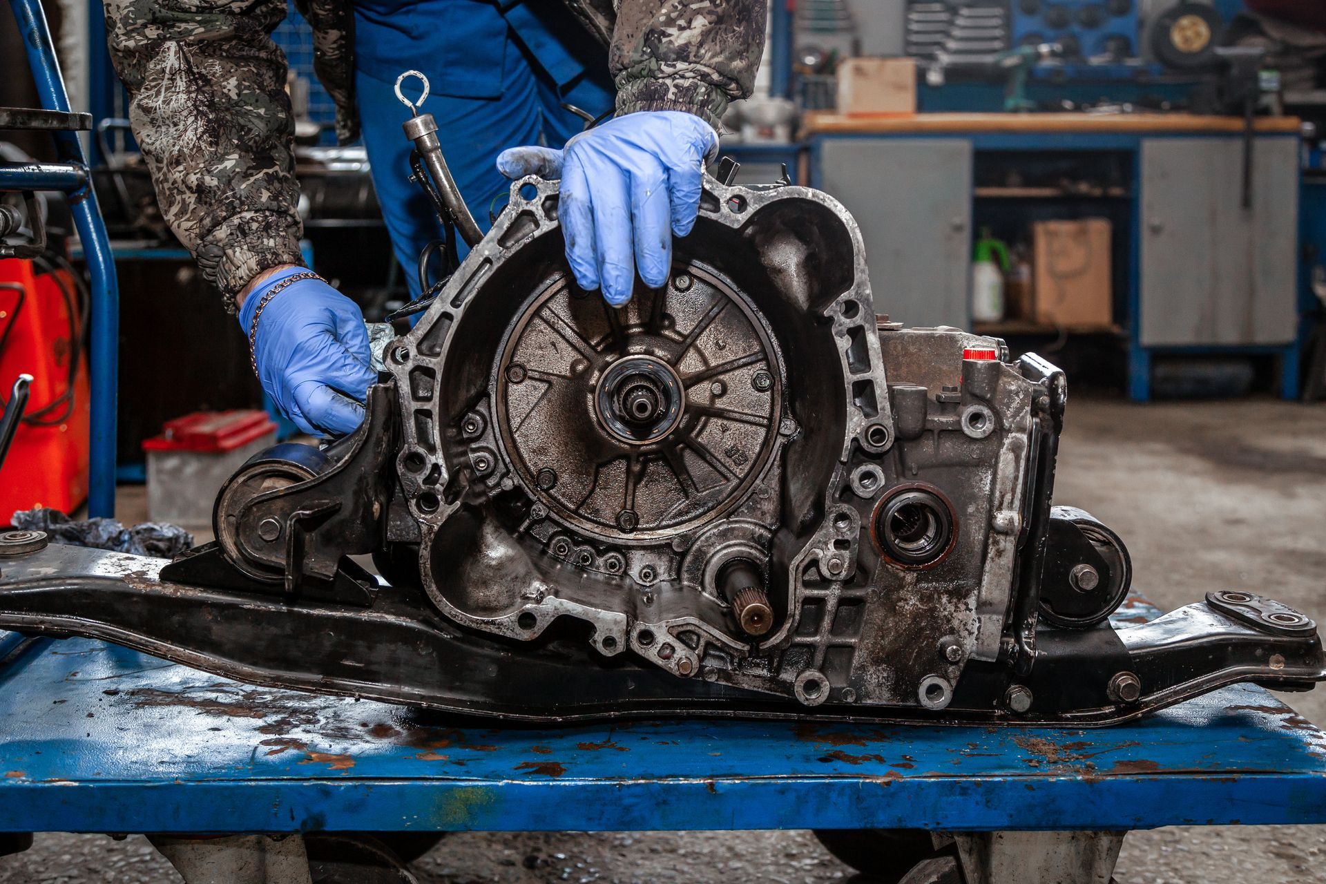Mechanic working on a greasy car transmission in a workshop, wearing blue gloves